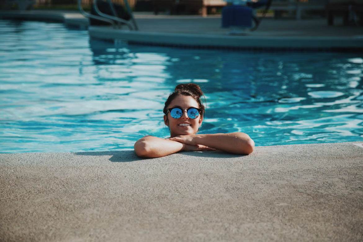 A woman with sunglasses perched at the edge of an outdoor pool