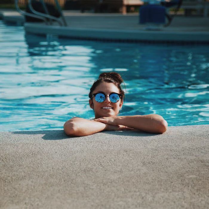 A woman with sunglasses perched at the edge of an outdoor pool